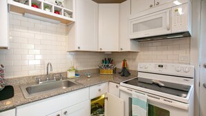 Una cocina con gabinetes blancos, encimera de granito, un lavamanos y dos hornos, además de un microondas.