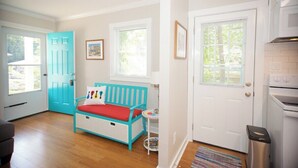 Una habitación luminosa con un sofá color turquesa, una puerta blanca y una zona de cocina.