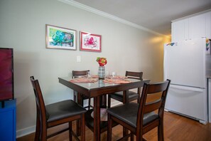 A dining area with a table set for four, surrounded by chairs, a refrigerator, and two framed artworks on the wall. - Two Spotless Homes Near Duke · Sleep 8 (Durham)