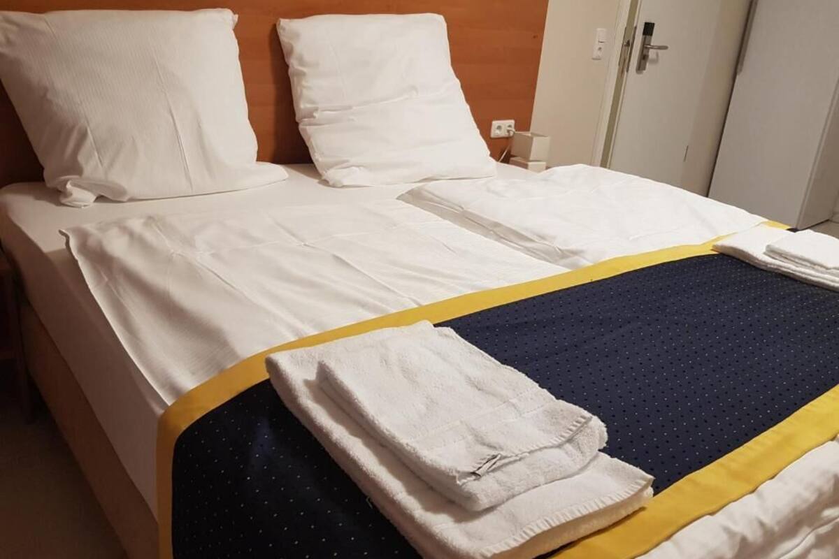Un lit bien fait, avec du linge de lit blanc et des touches de bleu et de jaune.