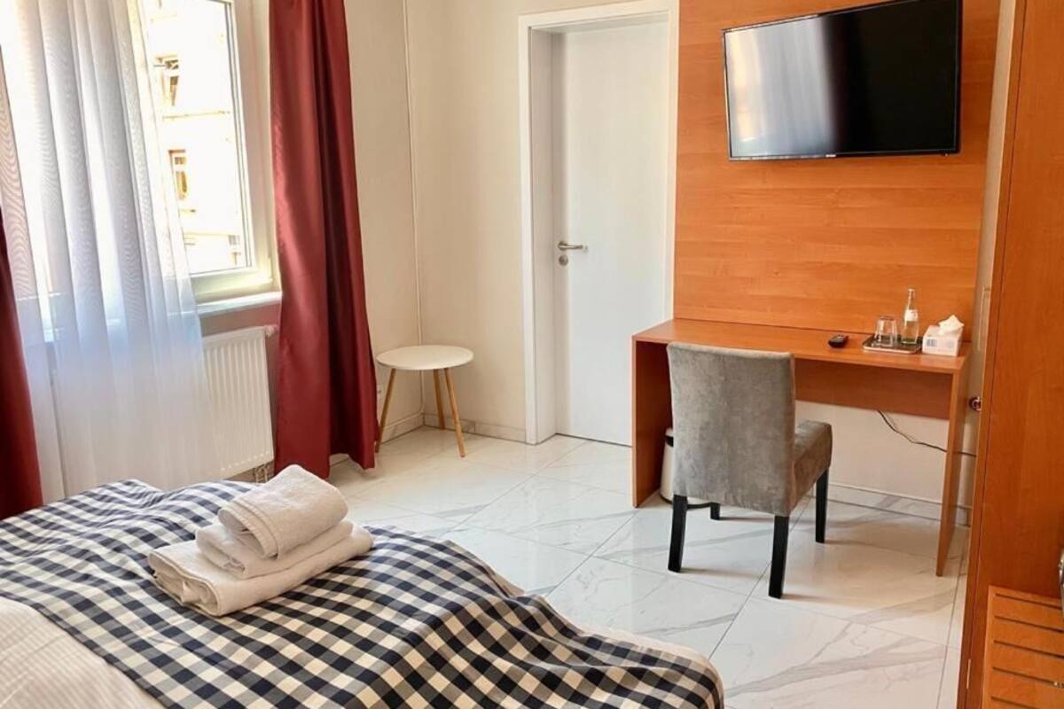 Une chambre d’hôtel avec un lit, un bureau, une chaise, une télévision et une fenêtre avec des rideaux.