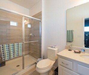 Uma casa de banho moderna com cabine de chuveiro em vidro, sanita, lavatório com espelho e suporte para toalhas.