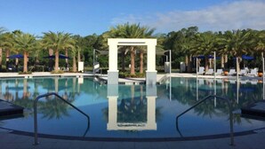 Une piscine aux eaux cristallines, surmontée d’une arche centrale et entourée de palmiers et de chaises longues.