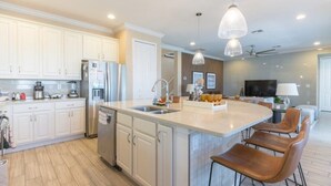 Une cuisine moderne avec des meubles blancs, un grand îlot central doté de tabourets, des appareils en acier inoxydable et un éclairage suspendu.