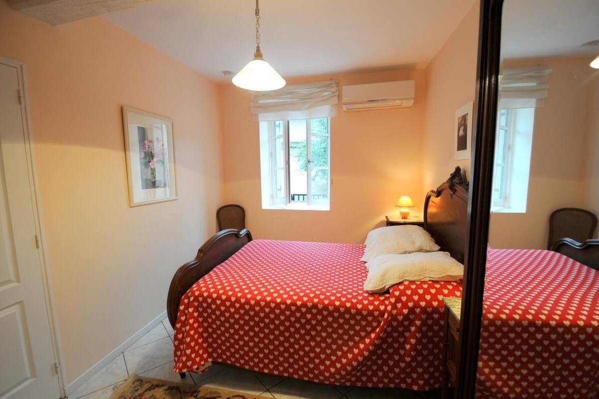 A bedroom with two beds, each with a red heart-patterned bedspread, a bedside lamp, and a window with white curtains.