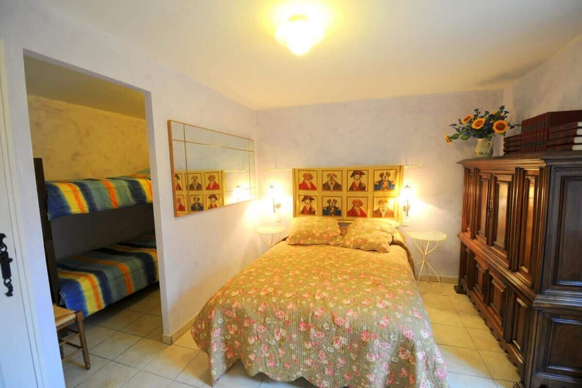 A bedroom with a single bed, a bunk bed, a mirror, framed pictures on the wall, a small table, and a cabinet.