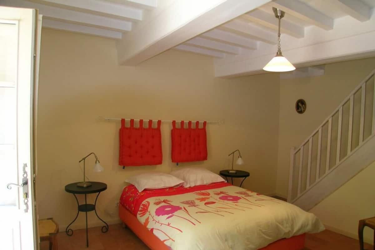 A bedroom with a bed, two nightstands, a red headboard, a staircase, and a door.