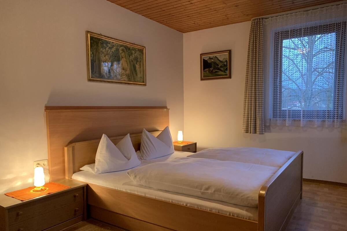 A neatly made bed with white linens and pillows, a wooden headboard, bedside lamps, and two framed artworks on the walls.