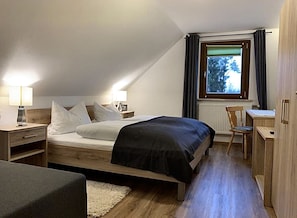 Un dormitorio con cama, mesitas de noche, un escritorio y una silla.