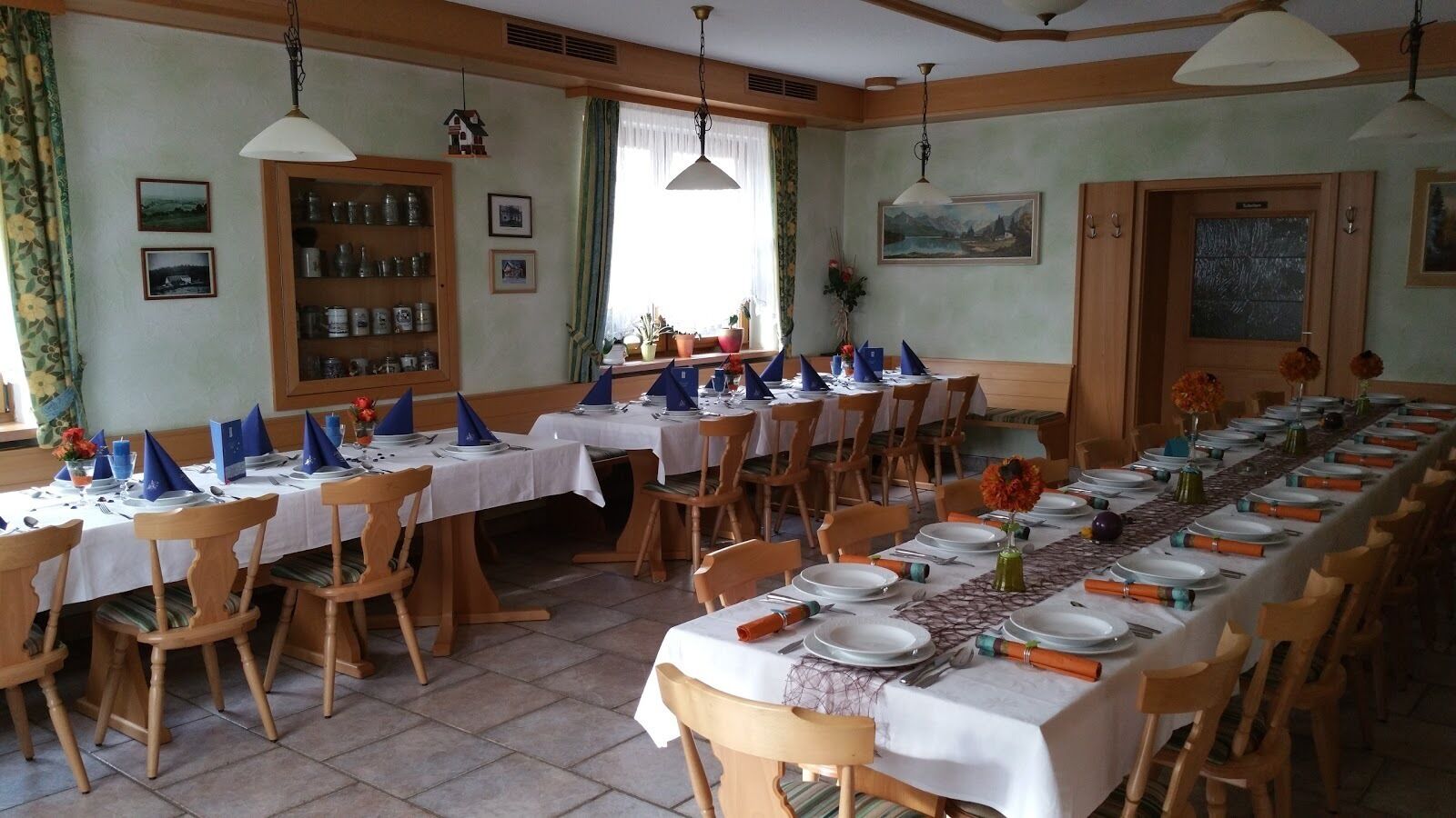 A dining hall with long tables set for a meal, wooden chairs, and a variety of table settings.