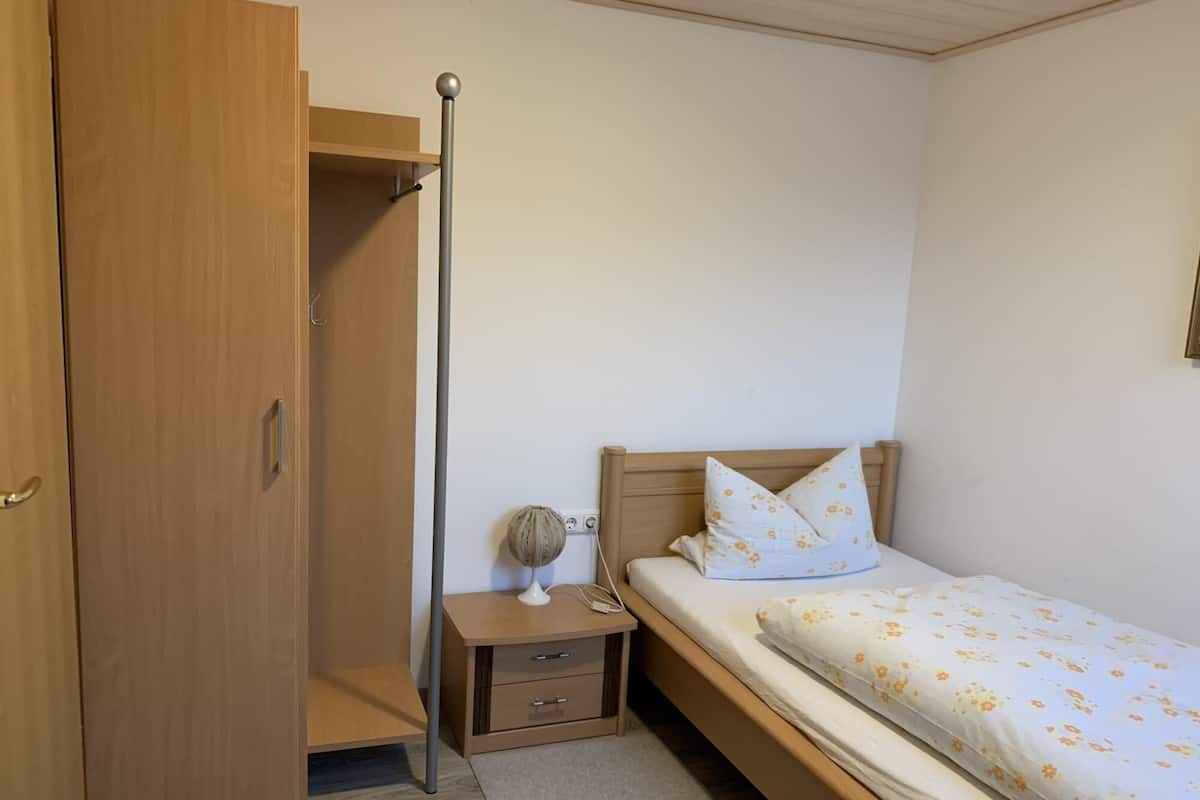 A bedroom with a wooden wardrobe, a bedside table with a lamp, and a bed with floral bedding.