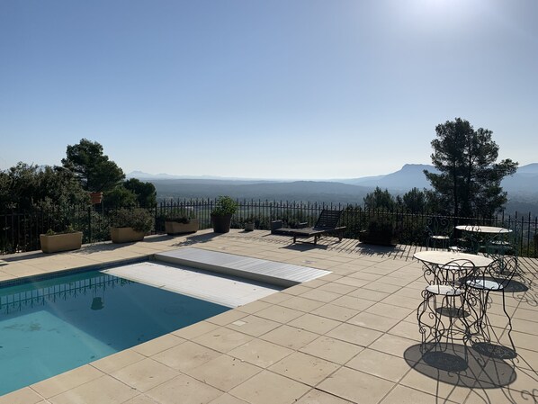 Un espace piscine aménagé sur le toit, offrant une vue sur les montagnes lointaines, et agrémenté de plantes en pot et de mobilier d’extérieur.
