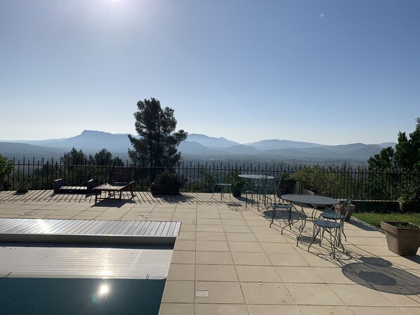 A rooftop terrace with a swimming pool, outdoor seating, and a view of distant mountains.