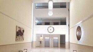 Un hall d’entrée spacieux avec un plafond haut, une grande horloge et un extincteur fixé au mur.