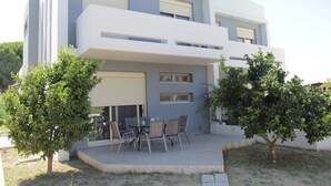 A modern two-story house with a flat roof, large windows, and a patio with outdoor furniture. - Platoni Elite Villas (Rhodes)