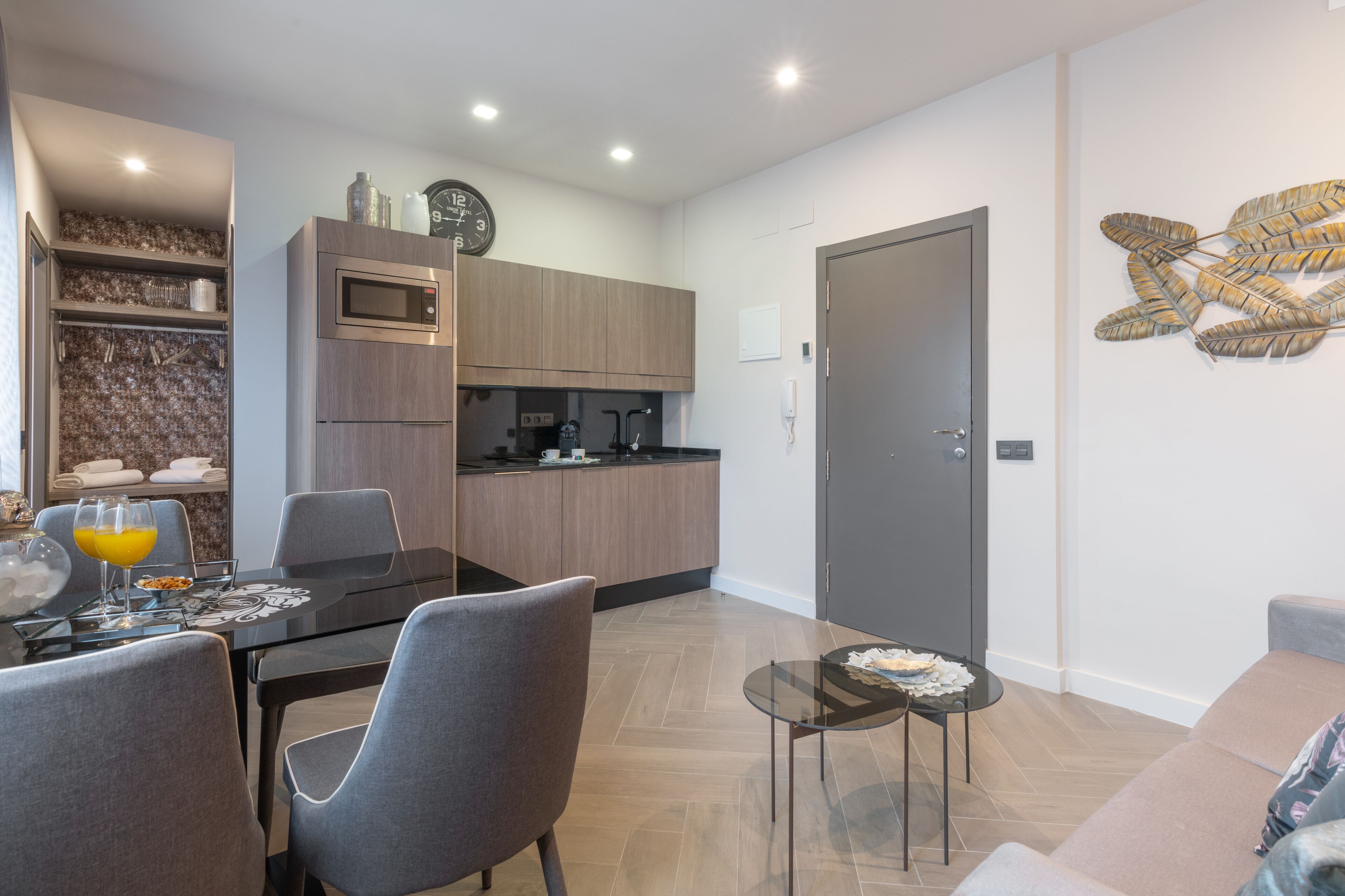 Uma cozinha moderna com eletrodomésticos embutidos, uma sala de jantar com mesa de vidro e uma área de estar com sofá e arte decorativa na parede.