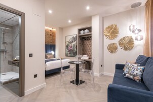 Une chambre d’hôtel moderne comprenant un lit, un coin salon avec une table et des chaises, un espace douche et des œuvres d’art décoratives au mur.