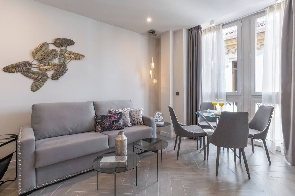 A modern living room with a grey sofa, a glass coffee table, and a dining area with a glass table and chairs.