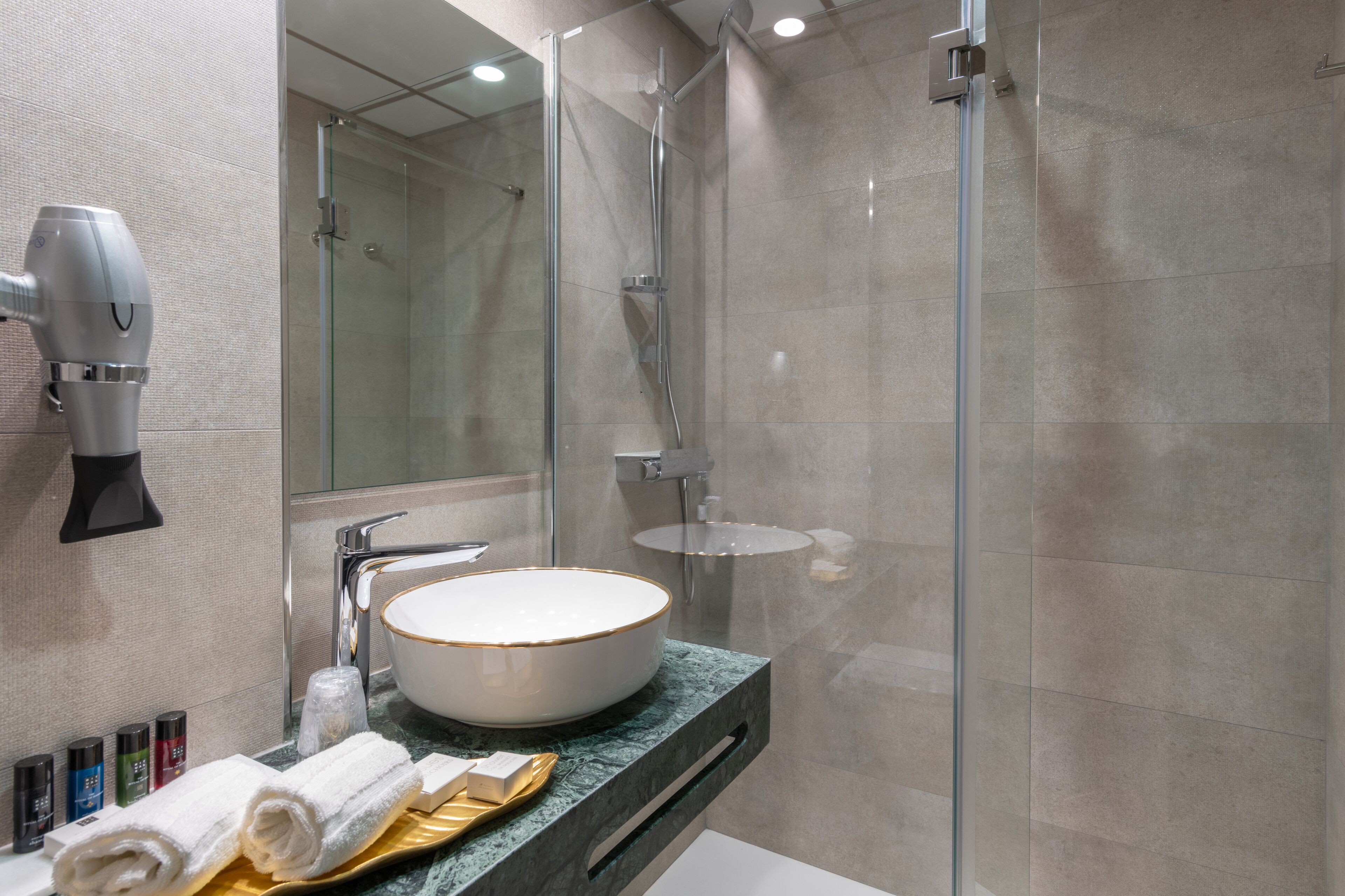 Un baño moderno con ducha acristalada, lavabo redondo y secador de pelo montado en la pared.