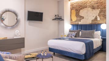 A modern bedroom with a brick accent wall, a flat-screen TV, a bedside table with decorative items, and a blue upholstered bed.