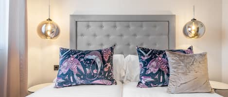 A neatly made bed with patterned pillows, a tufted headboard, and two spherical pendant lights.