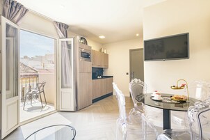 Una cocina moderna con horno empotrado, una zona de comedor con mesa y sillas de vidrio, y un televisor montado en la pared.