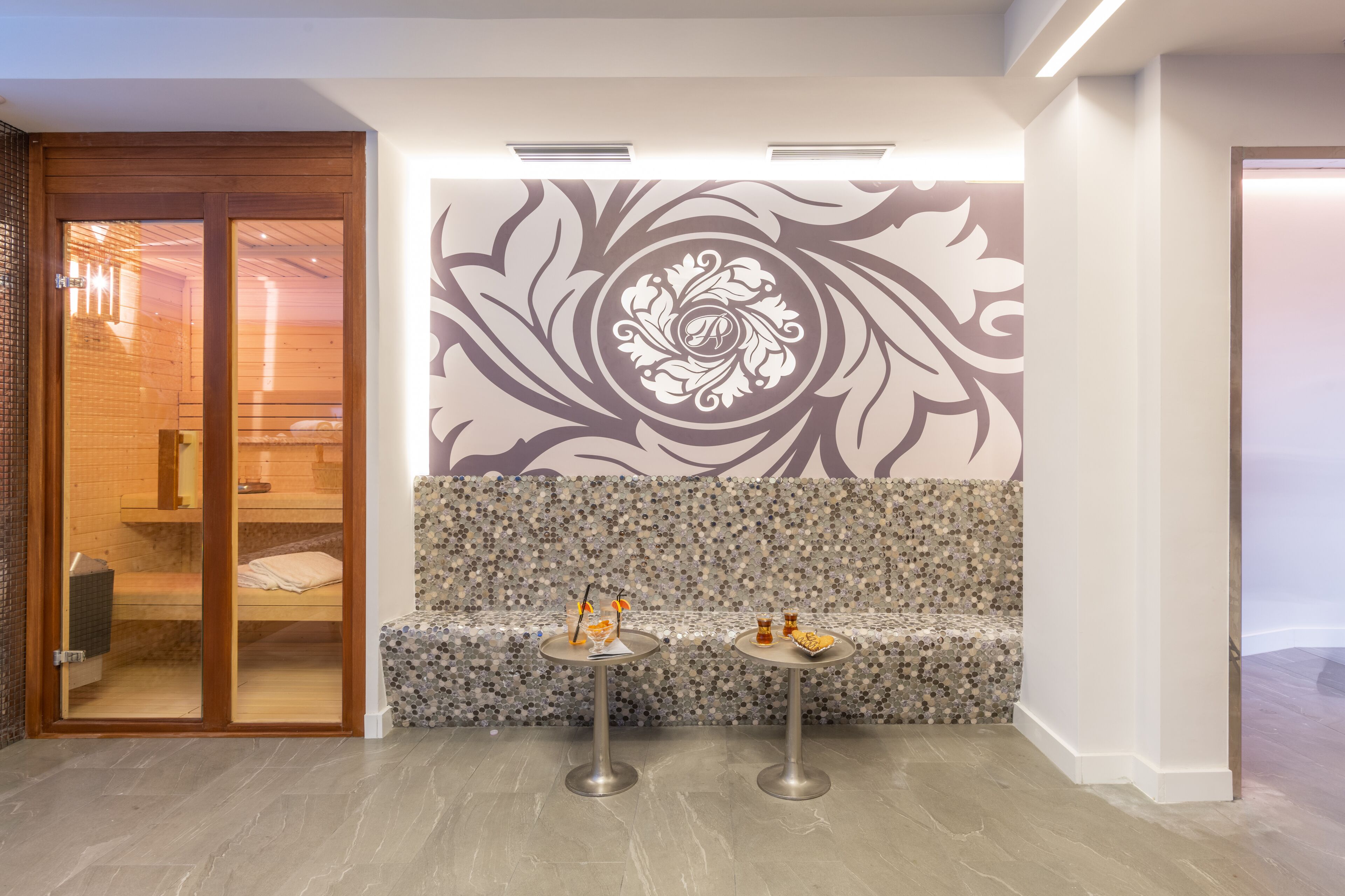 A modern lobby with a wooden bench, two small tables with decorative items, and a decorative wall mural.