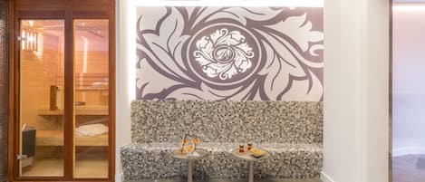 A modern lobby with a wooden bench, two small tables with decorative items, and a decorative wall mural.