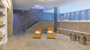 Moderni spa-alue, jossa on kaksi puista lepotuolia, pieni pöytä pyyhkeineen sekä lasiseinällä varustetut portaat.