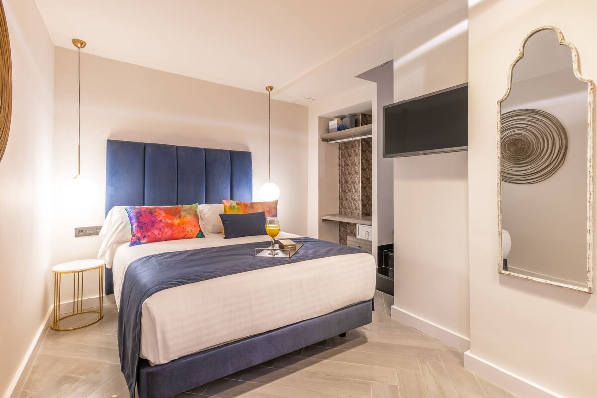 A modern bedroom with a large bed, bedside tables, a wardrobe, and a mirror.