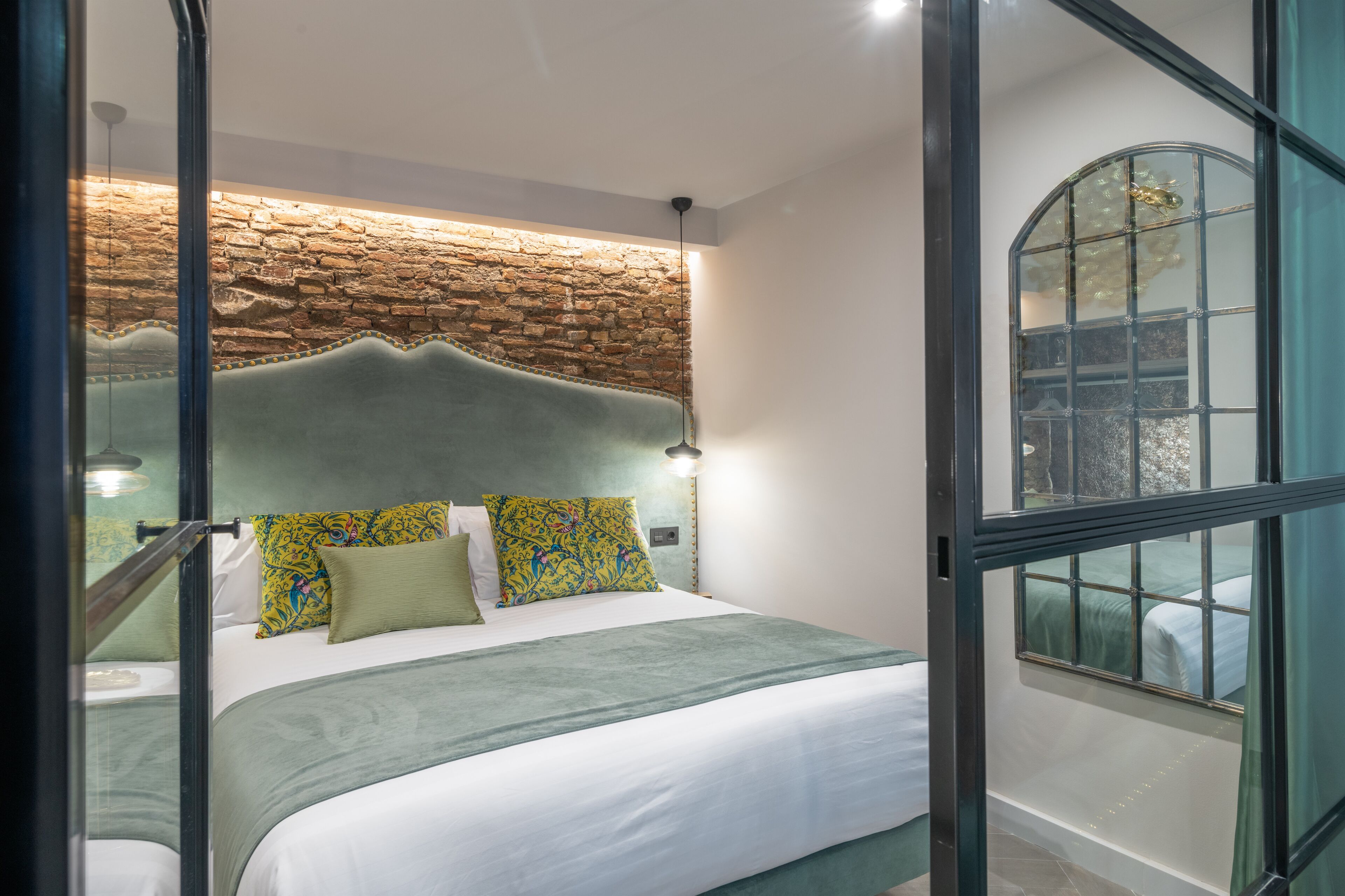 A modern bedroom with a stone wall, a large bed with patterned pillows, and a view through a glass door.