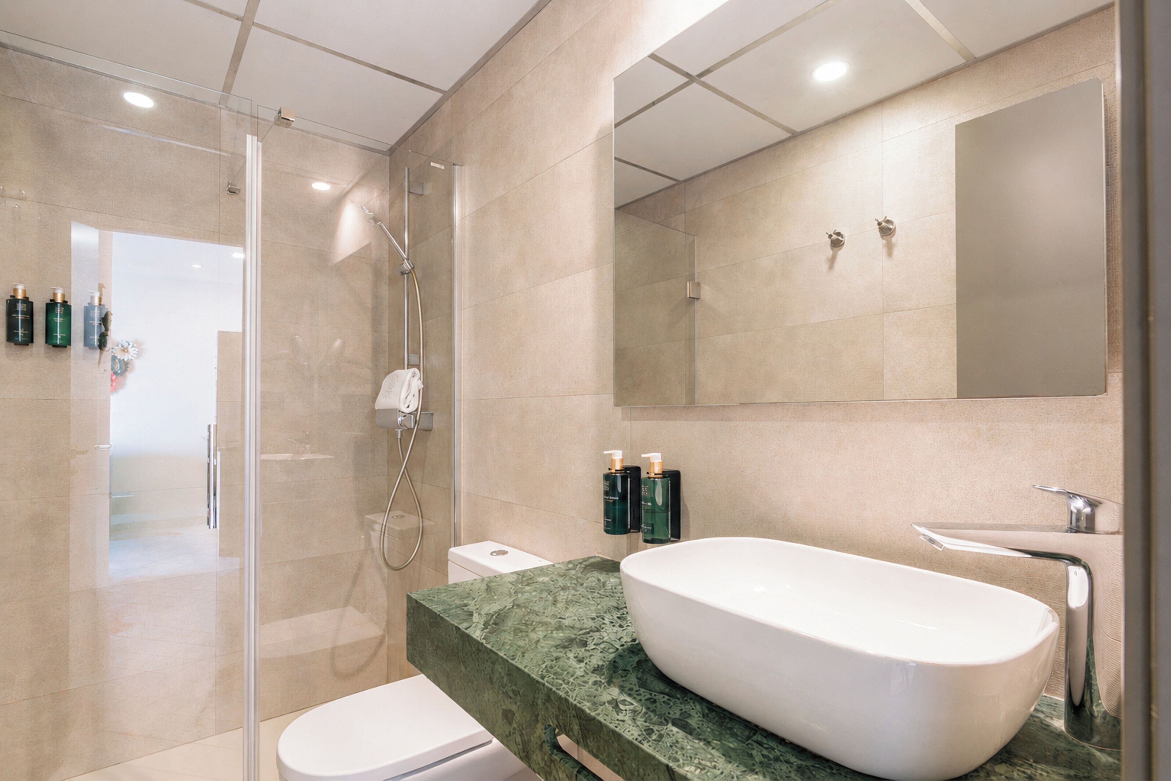 Un baño moderno con ducha de vidrio, lavamanos blanco y un espejo grande.