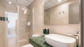 Un baño moderno con ducha de vidrio, lavamanos blanco y un espejo grande.