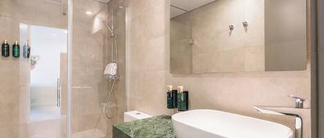 Un baño moderno con ducha de vidrio, lavamanos blanco y un espejo grande.