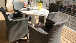 A balcony with wicker furniture, a table, a bottle of wine, and a vase with flowers.