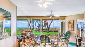 A dining area with a view of a golf course, a ceiling fan, and a painting on the wall. - Menehune 122 Beautiful Ocean Views in Beautiful Condo Home (Kihei)