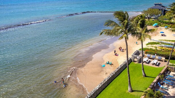 A beach with a stone wall, palm trees, and lounge chairs. - Menehune 122 Beautiful Ocean Views in Beautiful Condo Home (Kihei)
