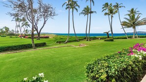 A well-maintained golf course with a clear view of the ocean and palm trees. - Menehune 122 Beautiful Ocean Views in Beautiful Condo Home (Kihei)