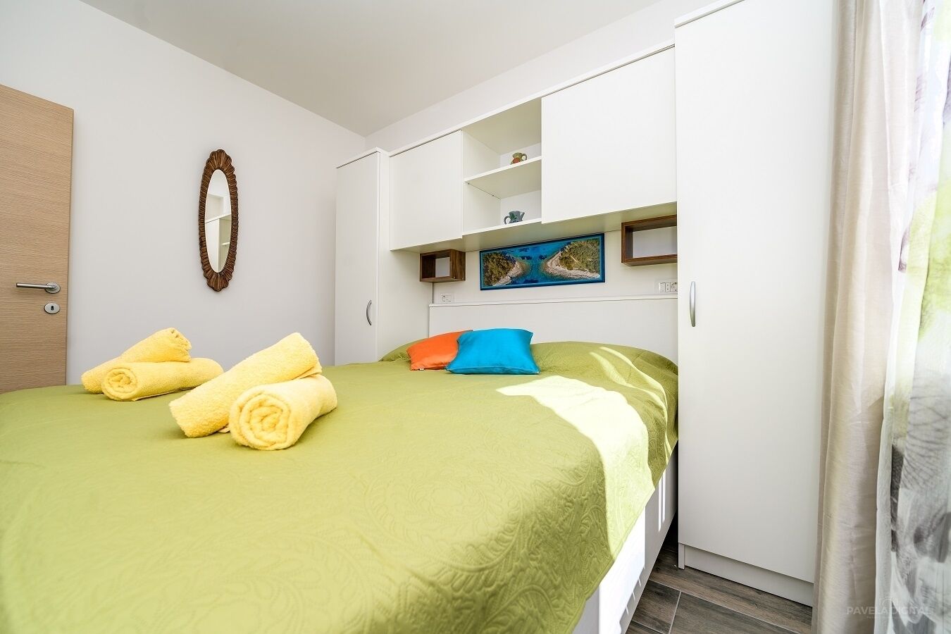 Una habitación de hotel con cama, armario, espejo y un cuadro en la pared.