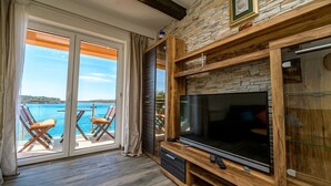 A spacious living room with a large TV, wooden entertainment unit, and a balcony with chairs overlooking a body of water. - Apartment in Mali Lošinj with Seaview, Balcony, Air condition, WIFI (4896-1) (Mali Lošinj)