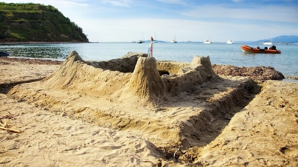 A sandy beach with a large sandcastle and boats in the background.