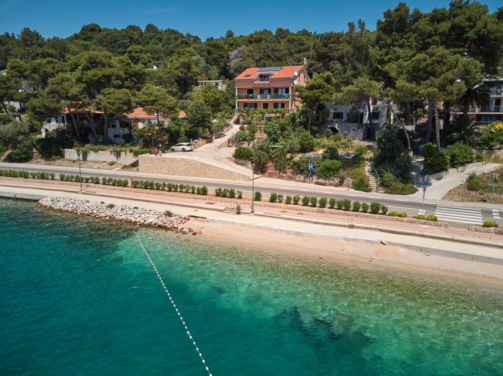 A coastal hotel with a clear view of the sea, a paved walkway, and lush greenery.