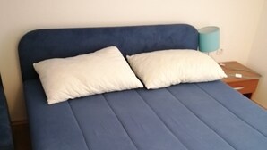 Ein Bett mit blauer Matratze und zwei weißen Kissen, ein Nachttisch aus Holz mit einer Lampe und ein Holzboden.