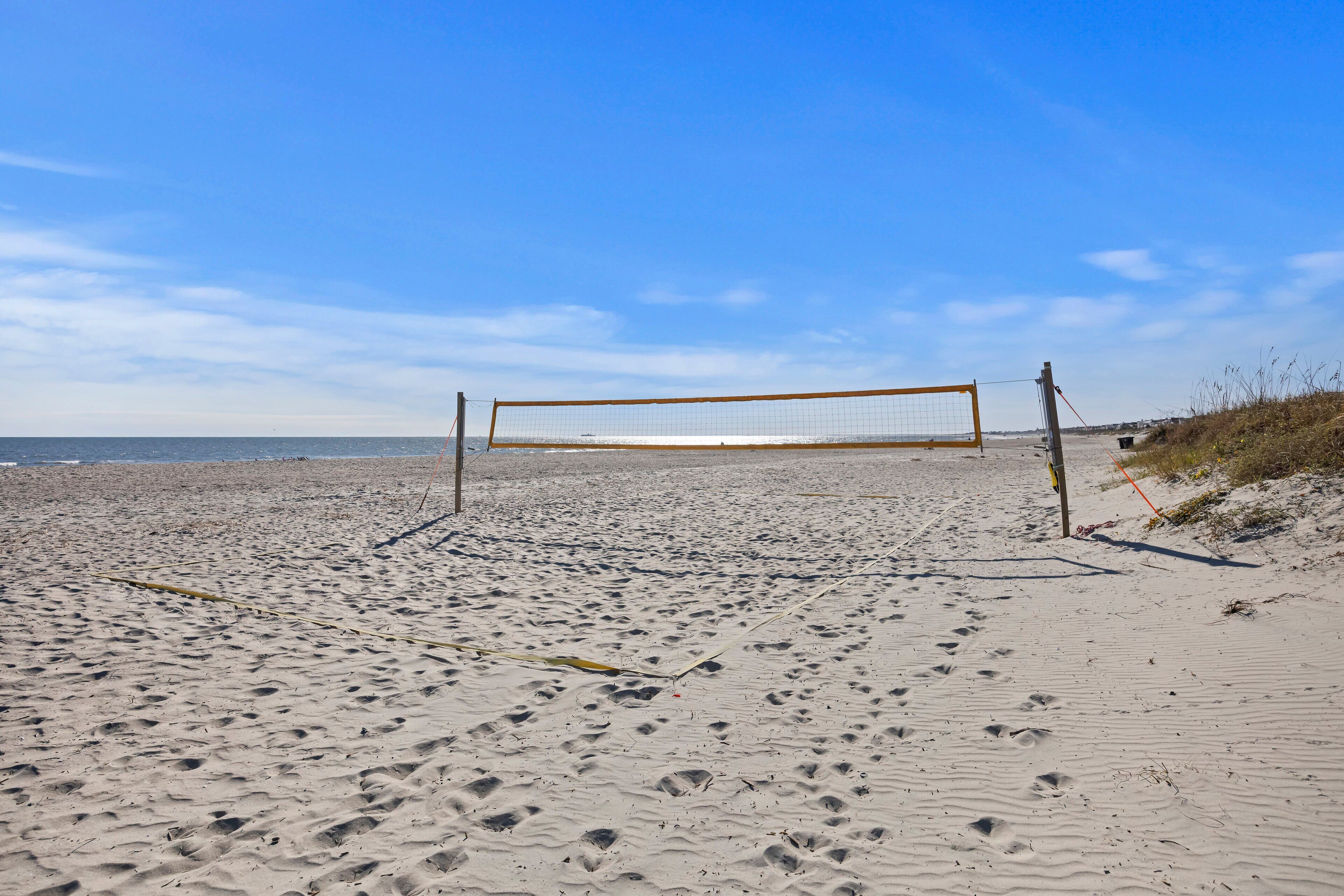Un filet de volley-ball sur une plage de sable, avec des empreintes de pas et un ciel dégagé.
