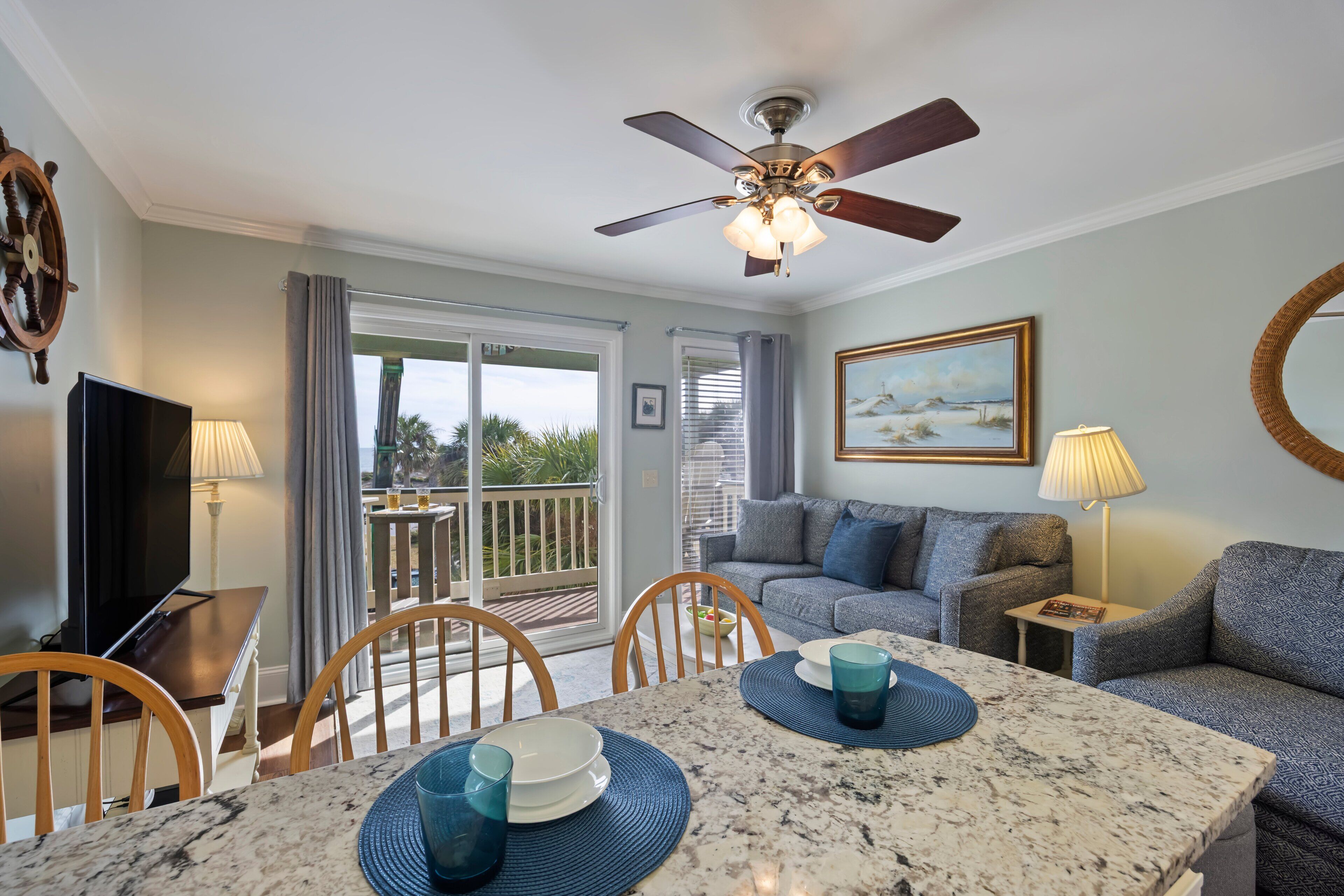 Un salon avec un ventilateur de plafond, un téléviseur, une table à manger avec des chaises, un canapé et un tableau accroché au mur.