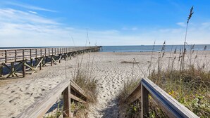 Une jetée en bois s’étendant sur une plage de sable, sous un ciel dégagé.