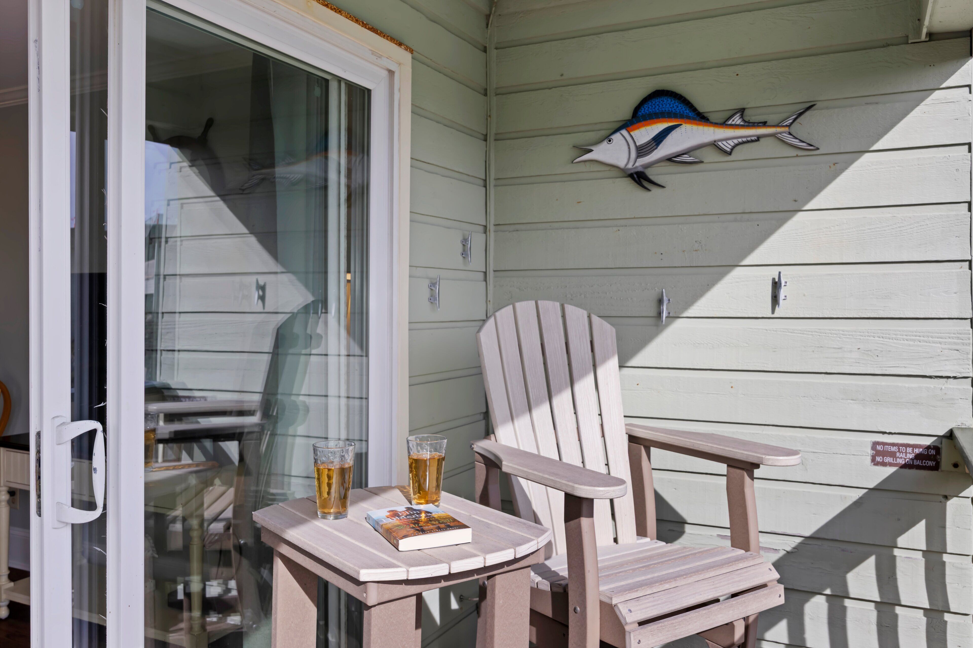 A wooden deck with a table and two chairs, a book, and two glasses of beer.