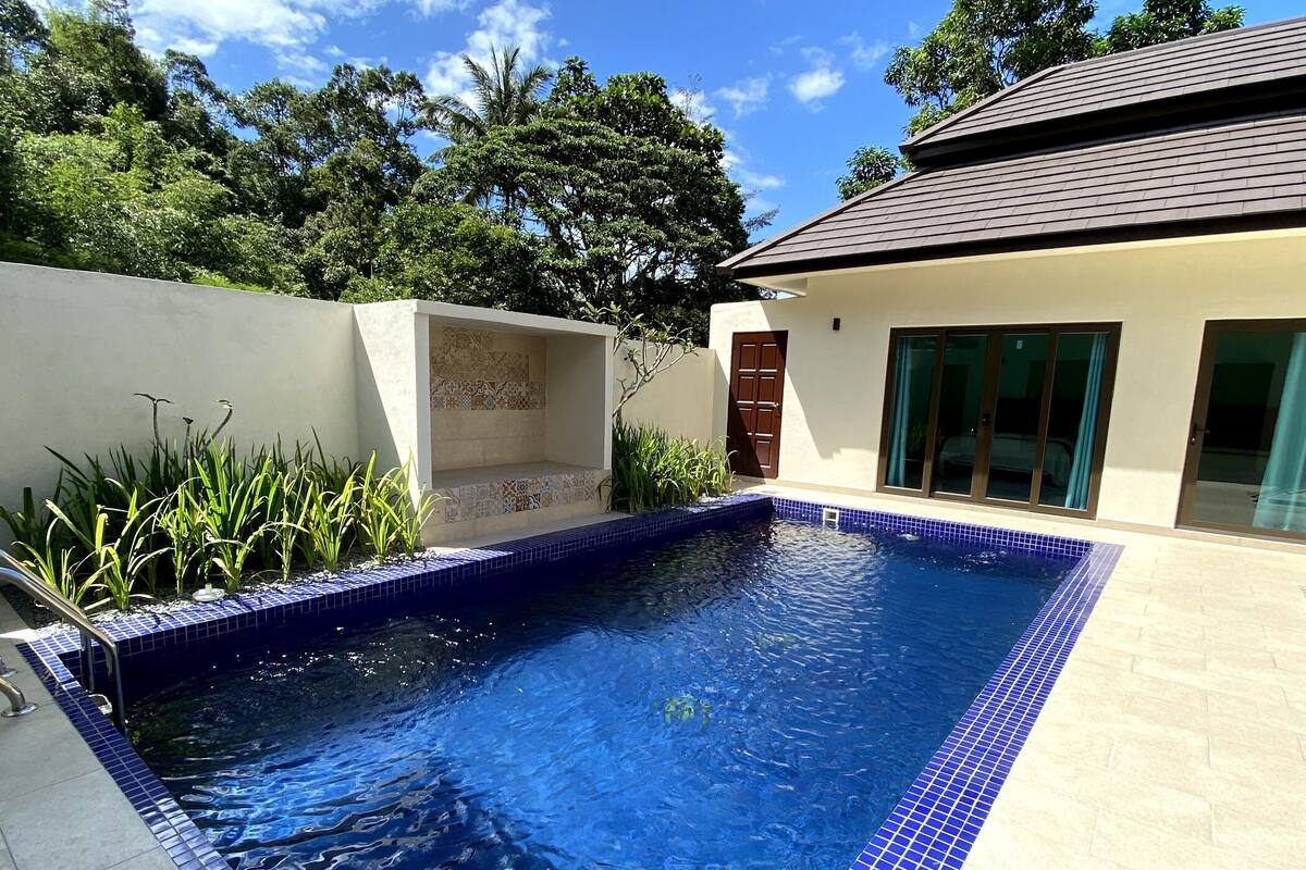 Una piscina con piastrelle blu, una panchina piastrellata e una casa con tetto e porta in piastrelle.