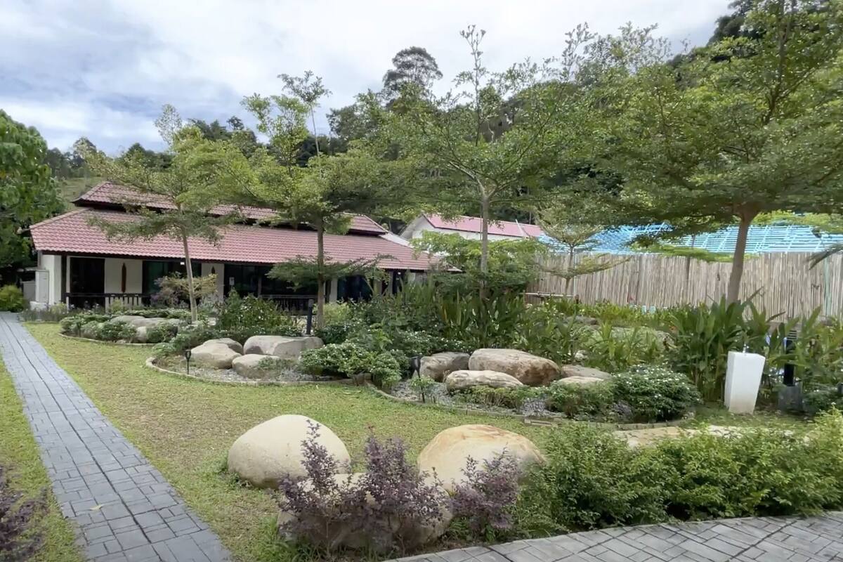 Un giardino con vialetto lastricato, grandi massi e un edificio con tetto rosso.