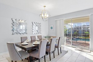 Een eetgedeelte met een grote tafel, zes stoelen en een kroonluchter.